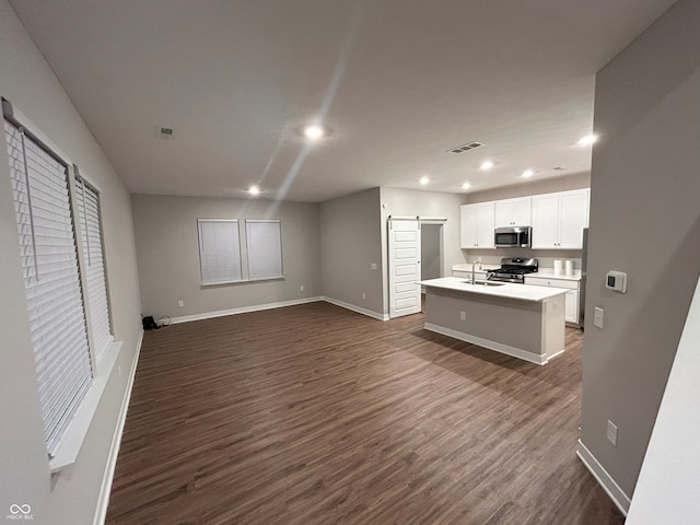 kitchen with dark hardwood / wood-style flooring, stainless steel appliances, a kitchen island with sink, a barn door, and white cabinetry