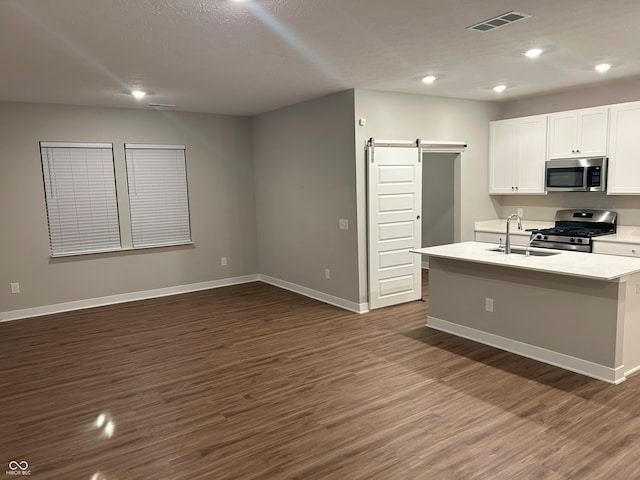 kitchen featuring stainless steel appliances, sink, a barn door, dark hardwood / wood-style floors, and an island with sink