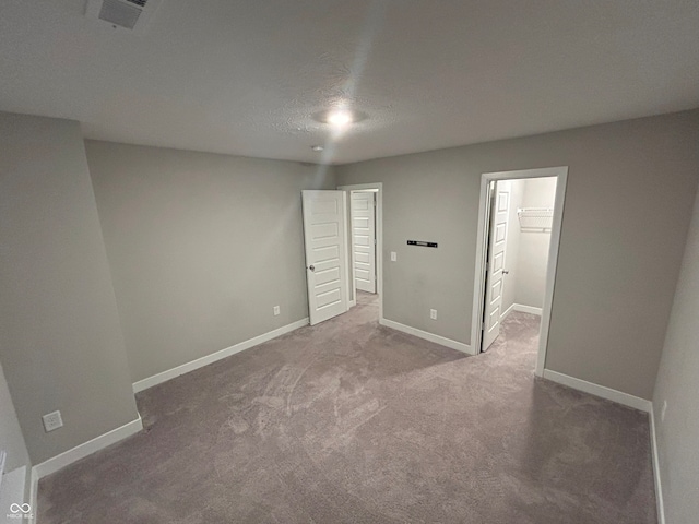 unfurnished bedroom featuring a walk in closet, a closet, carpet floors, and a textured ceiling