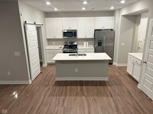 kitchen featuring a barn door, dark hardwood / wood-style flooring, stainless steel appliances, and an island with sink