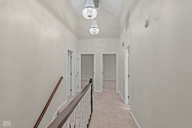 corridor featuring light carpet, high vaulted ceiling, and a notable chandelier