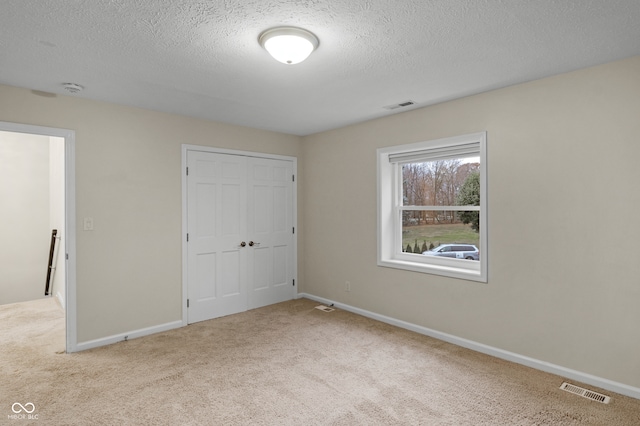 unfurnished bedroom with light carpet, a closet, and a textured ceiling