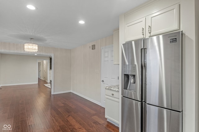 kitchen with light stone countertops, an inviting chandelier, dark hardwood / wood-style flooring, stainless steel fridge, and white cabinets