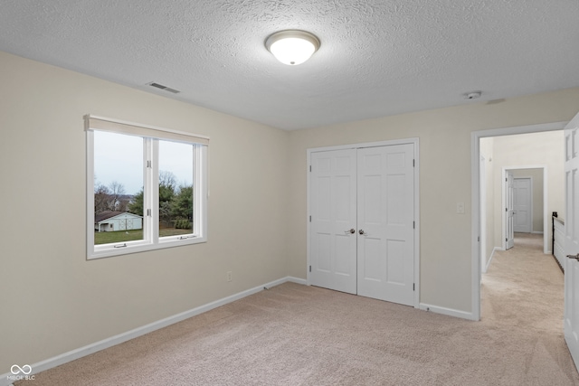 unfurnished bedroom with light colored carpet, a textured ceiling, and a closet