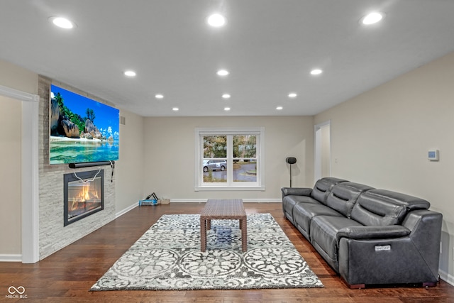 living room featuring a stone fireplace and dark wood-type flooring