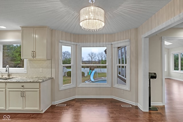 unfurnished dining area with a textured ceiling, an inviting chandelier, dark wood-type flooring, and sink