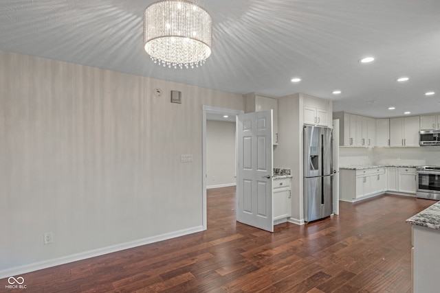 kitchen featuring light stone countertops, appliances with stainless steel finishes, dark hardwood / wood-style flooring, white cabinets, and a chandelier