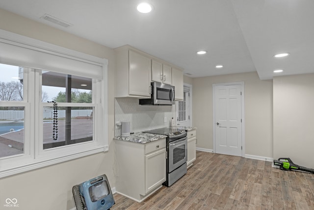 kitchen with light stone counters, white cabinetry, stainless steel appliances, and light hardwood / wood-style flooring