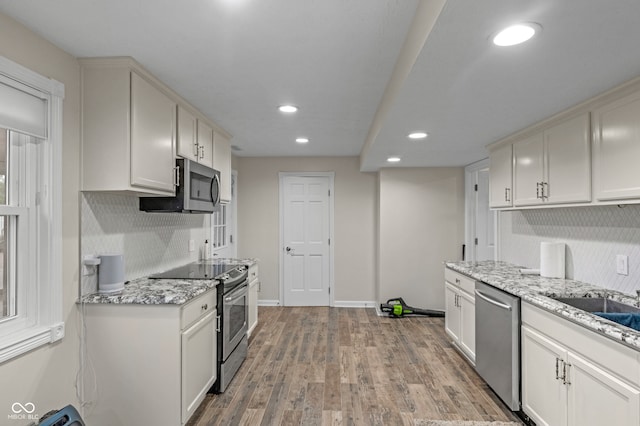 kitchen featuring white cabinetry, light stone countertops, light wood-type flooring, and stainless steel appliances