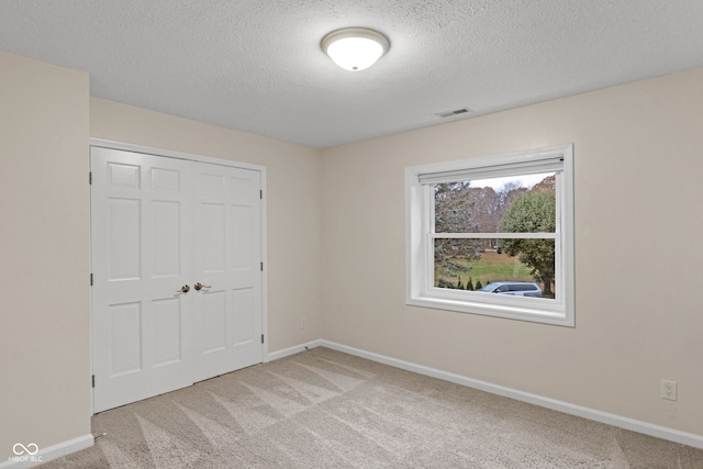 unfurnished bedroom featuring a textured ceiling, light colored carpet, and a closet