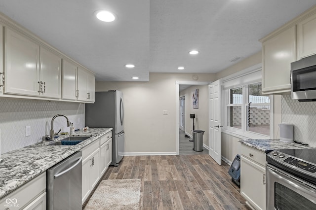 kitchen featuring light stone countertops, appliances with stainless steel finishes, backsplash, sink, and wood-type flooring