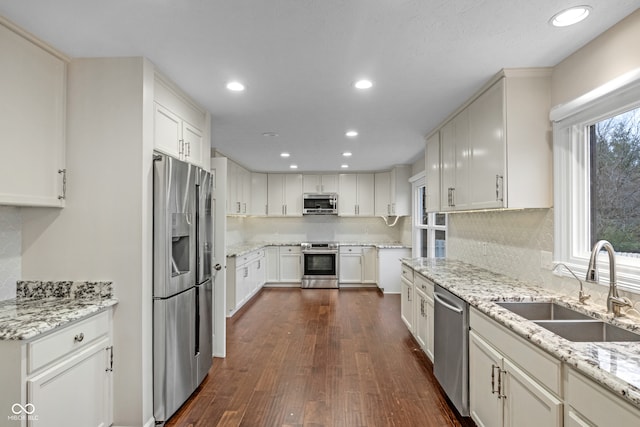 kitchen with dark hardwood / wood-style flooring, light stone counters, stainless steel appliances, sink, and white cabinetry