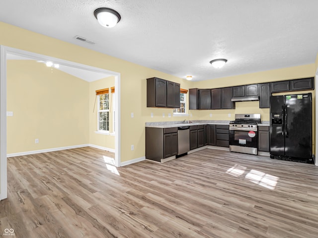 kitchen featuring dark brown cabinets, light wood-type flooring, stainless steel appliances, and a textured ceiling