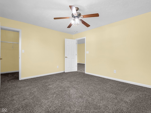 unfurnished bedroom with dark colored carpet, ceiling fan, a spacious closet, and a closet