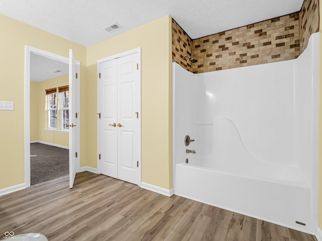 bathroom featuring hardwood / wood-style floors, shower / bathing tub combination, and a textured ceiling