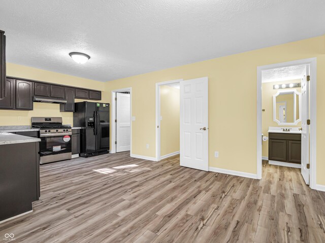 11411 Shady Hollow Ln, Indianapolis, IN 46229 - kitchen with black fridge, gas stove, under cabinet range hood, light wood-type flooring, and a textured ceiling