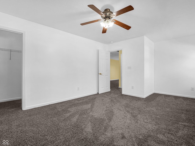 unfurnished bedroom with a walk in closet, a closet, dark carpet, and ceiling fan