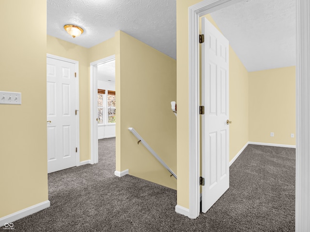 hallway featuring dark colored carpet and a textured ceiling