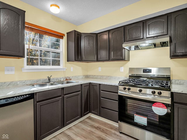 kitchen featuring appliances with stainless steel finishes, dark brown cabinetry, light hardwood / wood-style floors, and a textured ceiling