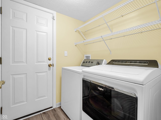 laundry area with independent washer and dryer, light wood-type flooring, and a textured ceiling