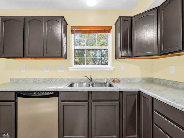 kitchen with a textured ceiling, dark brown cabinetry, stainless steel dishwasher, and sink