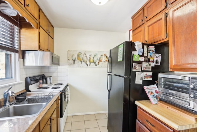 kitchen featuring range with electric stovetop, sink, decorative backsplash, exhaust hood, and black fridge