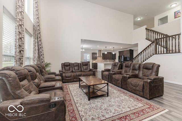 living room with an inviting chandelier, a healthy amount of sunlight, a high ceiling, and light hardwood / wood-style floors