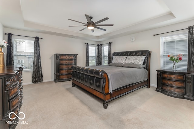 bedroom featuring light colored carpet, a raised ceiling, multiple windows, and ceiling fan