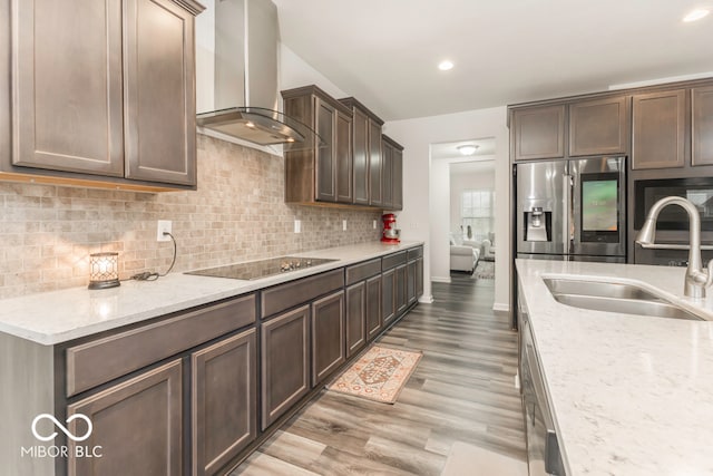 kitchen with sink, wall chimney exhaust hood, light stone counters, light hardwood / wood-style floors, and appliances with stainless steel finishes