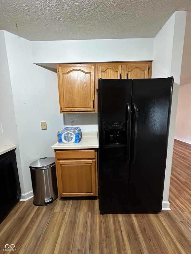 kitchen featuring black refrigerator with ice dispenser, hardwood / wood-style floors, and a textured ceiling