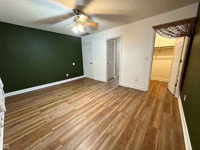 unfurnished bedroom featuring ceiling fan, a spacious closet, hardwood / wood-style floors, a textured ceiling, and a closet