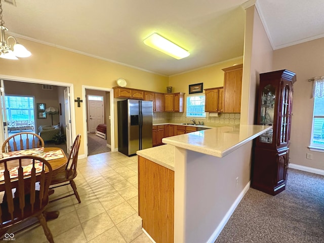 kitchen with hanging light fixtures, tasteful backsplash, kitchen peninsula, stainless steel fridge, and crown molding