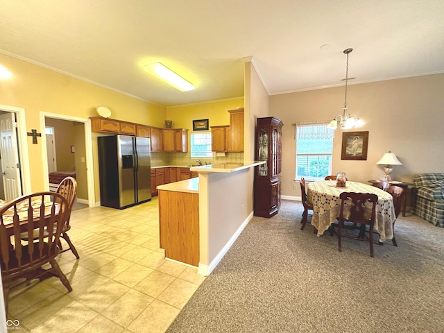 kitchen featuring hanging light fixtures, an inviting chandelier, kitchen peninsula, stainless steel fridge, and crown molding