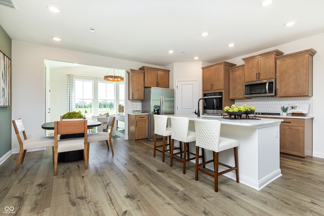 kitchen with a breakfast bar, tasteful backsplash, a center island with sink, light wood-type flooring, and stainless steel appliances