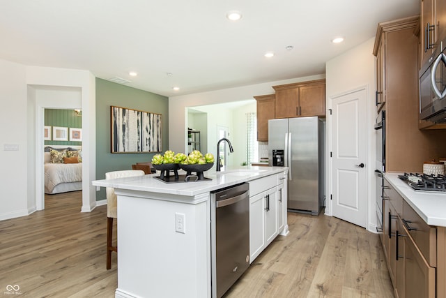 kitchen with appliances with stainless steel finishes, white cabinetry, sink, a kitchen island with sink, and light hardwood / wood-style flooring