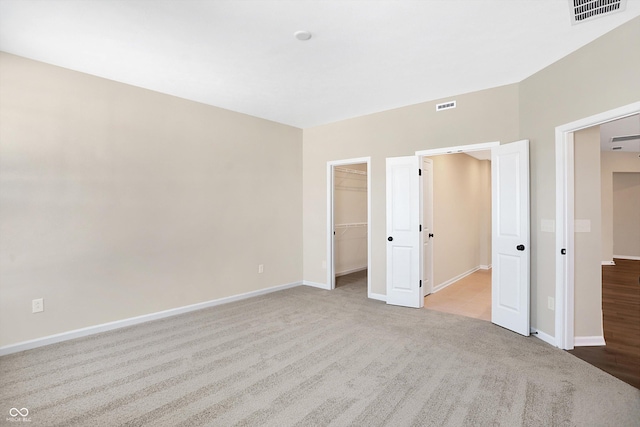 unfurnished bedroom with a spacious closet, light carpet, and a closet