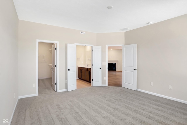 unfurnished bedroom featuring a spacious closet, light colored carpet, a closet, and ensuite bathroom