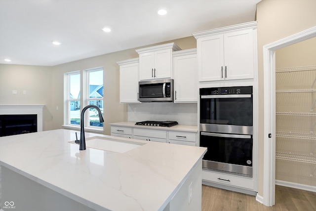 kitchen with appliances with stainless steel finishes, sink, white cabinets, and light hardwood / wood-style flooring