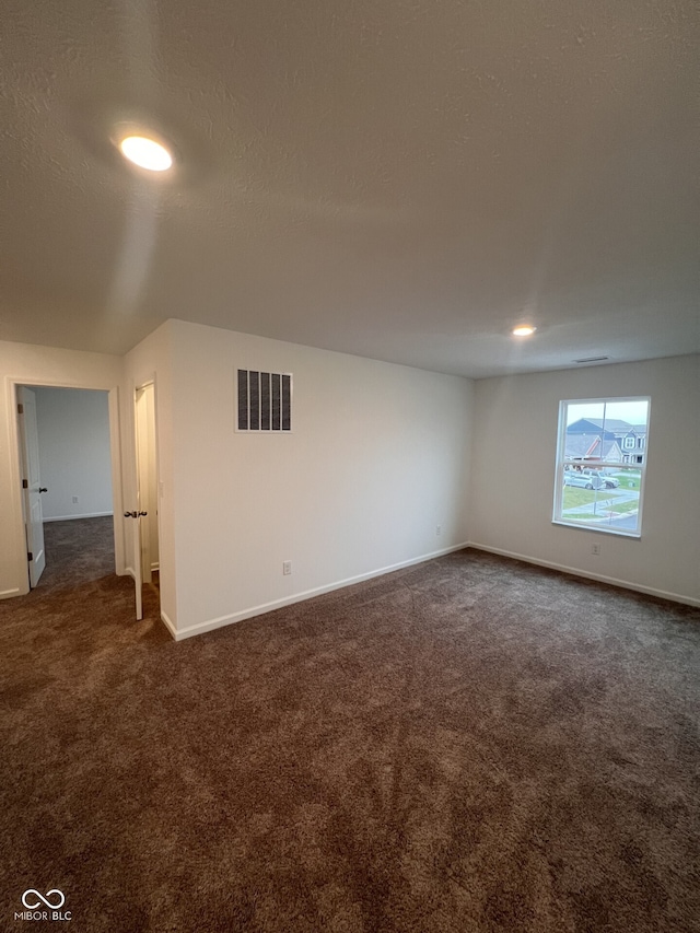 spare room featuring a textured ceiling and dark carpet