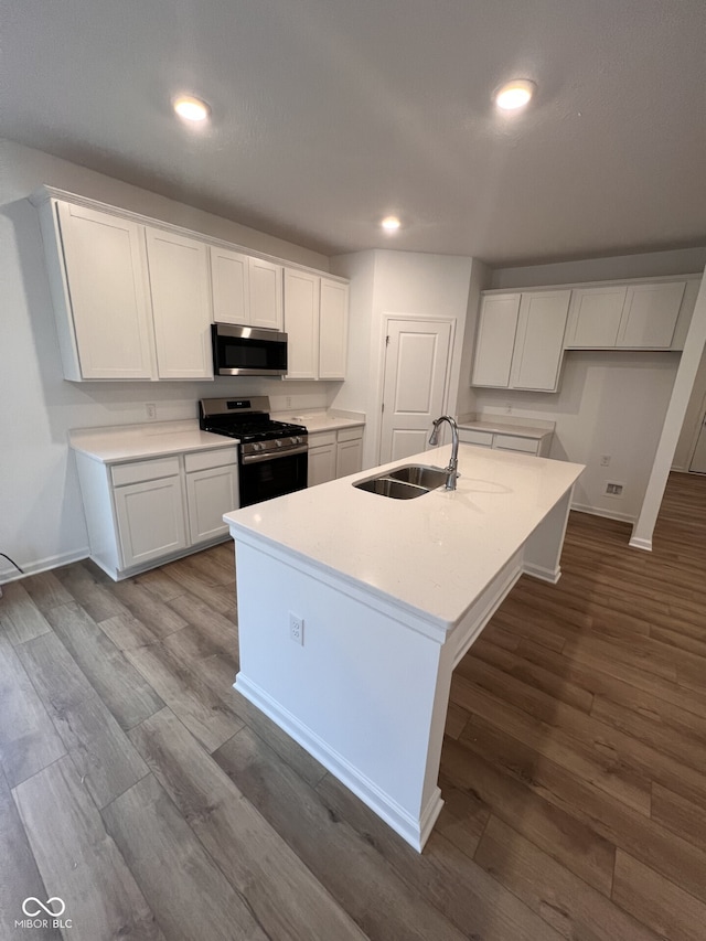 kitchen with white cabinetry, sink, a center island with sink, appliances with stainless steel finishes, and hardwood / wood-style flooring