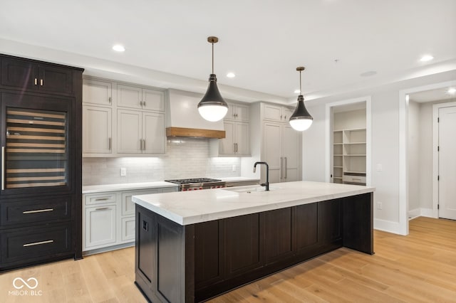 kitchen featuring pendant lighting, a center island with sink, sink, light hardwood / wood-style flooring, and light stone counters