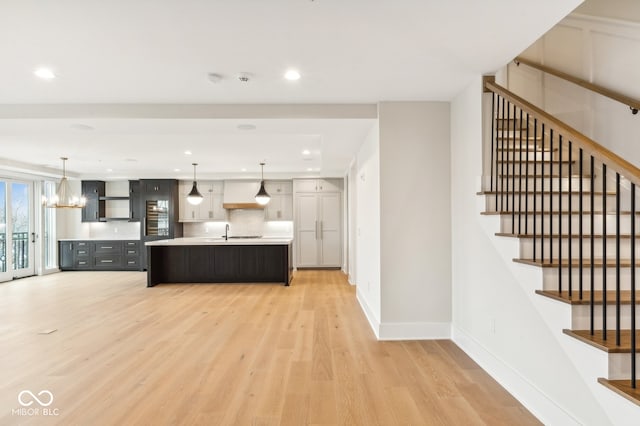 kitchen featuring light wood-type flooring, a kitchen island with sink, sink, pendant lighting, and a notable chandelier