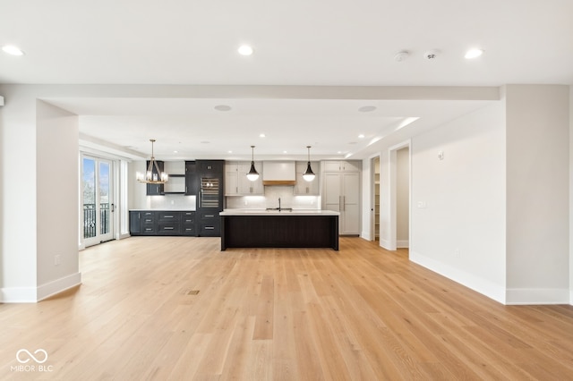 kitchen featuring decorative light fixtures, sink, light wood-type flooring, and a kitchen island with sink