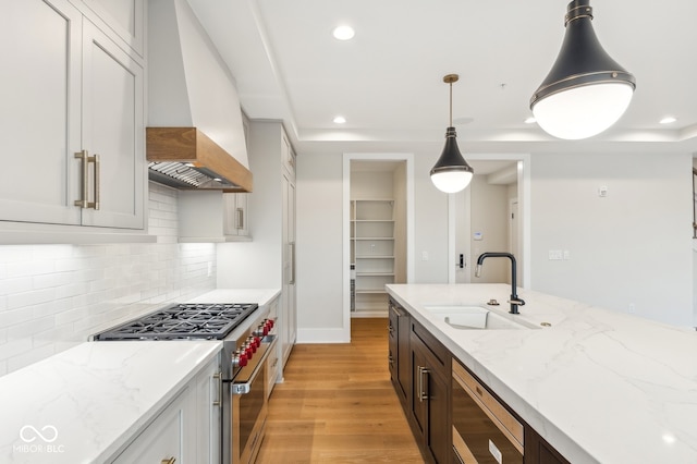 kitchen featuring custom range hood, stainless steel appliances, sink, decorative light fixtures, and light hardwood / wood-style floors