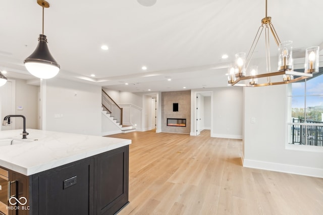 kitchen featuring a tile fireplace, sink, hanging light fixtures, light hardwood / wood-style flooring, and light stone counters