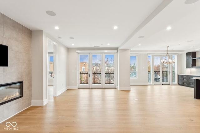 unfurnished living room featuring a tile fireplace, light hardwood / wood-style flooring, and a notable chandelier