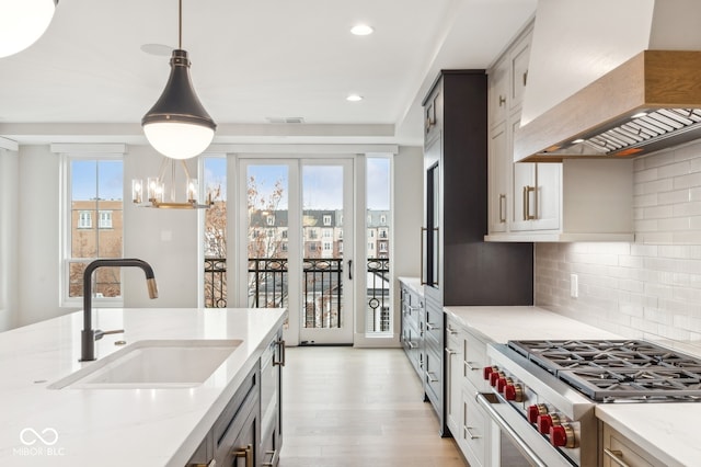 kitchen featuring light stone countertops, custom range hood, sink, decorative light fixtures, and high end stainless steel range