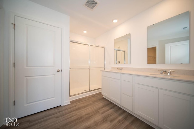 bathroom with wood finished floors, a sink, visible vents, and a shower stall