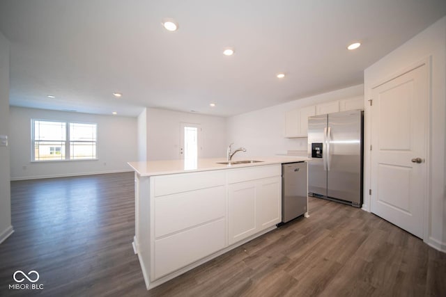 kitchen with stainless steel appliances, light countertops, white cabinets, a sink, and an island with sink