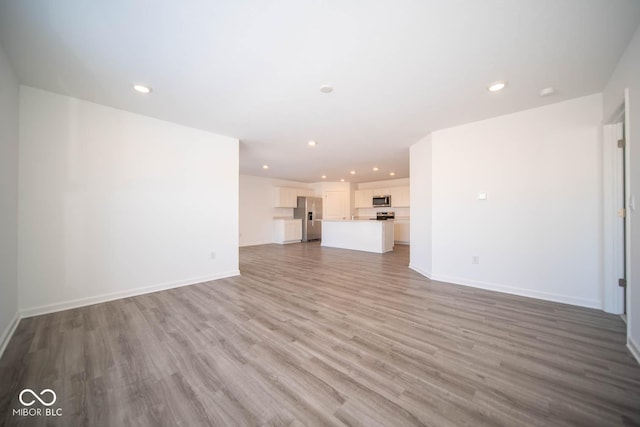 unfurnished living room with recessed lighting, wood finished floors, and baseboards